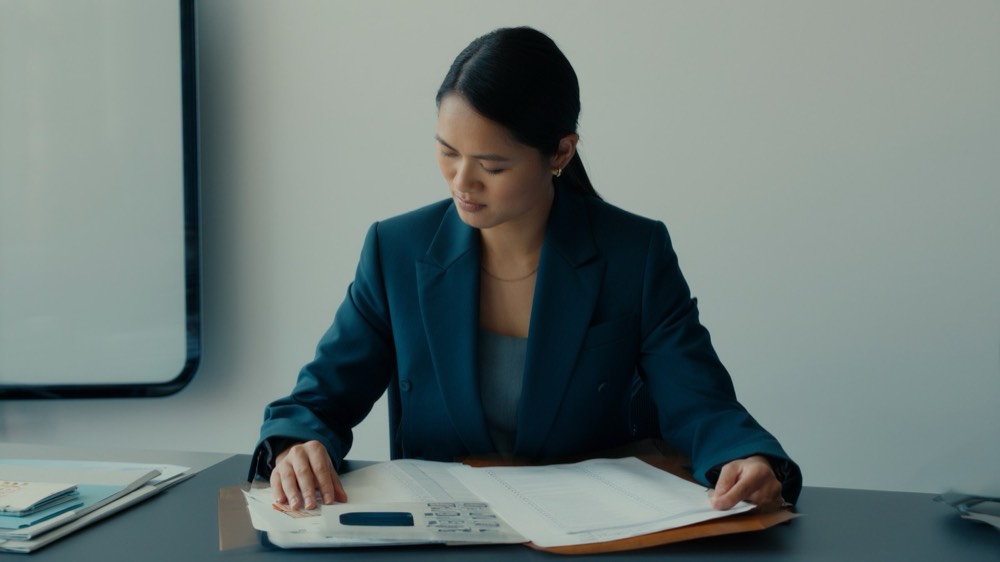 Real estate professional reviewing compliance paperwork at a desk with a laptop